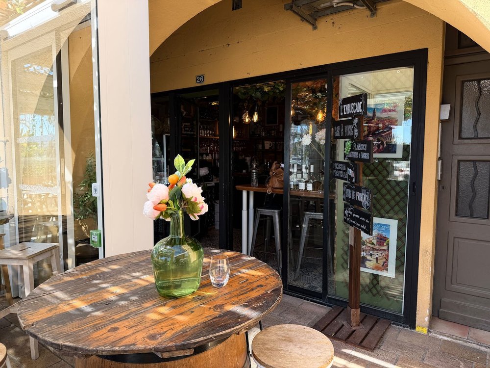 L'entrée du bar à vin L'Embuscade, une table en bois et un bouquet devant la porte